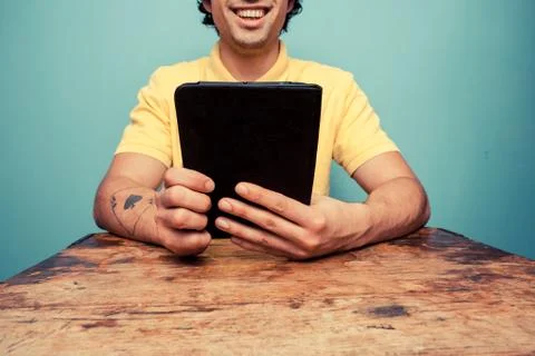 Young man at table reading on tablet Photos