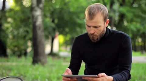 The Young Man With the Tablet Computer on a Bench in the Park Video stock 50994964