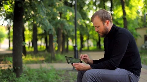 The Young Man With the Tablet Computer on a Bench in the Park Video stock 50994975