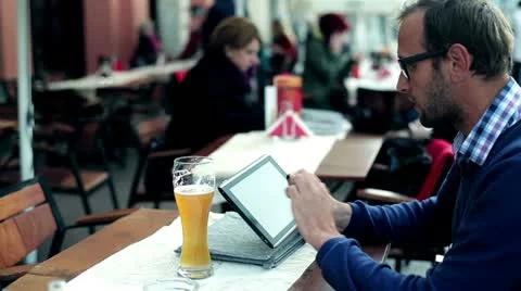 Young man with tablet computer drinking beer in the restaurant, outdoors 스톡 동영상 12380396