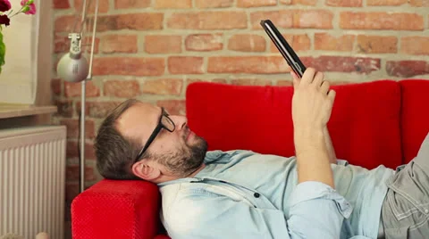 Young man with tablet computer lying on sofa HD Stock Footage 26283116