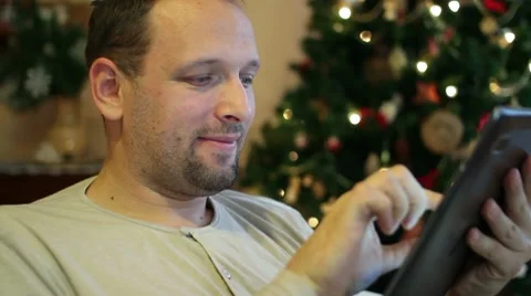 Young man with tablet computer on sofa, christmas tree in background Stock Footage 10741898