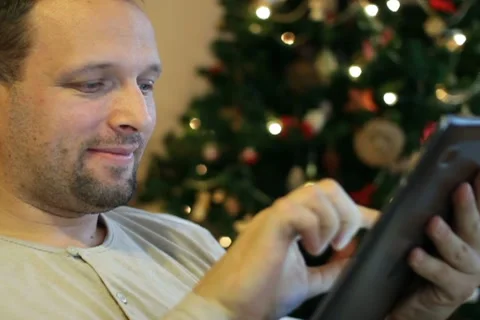 Young man with tablet computer on sofa, christmas tree in background Stock Footage 10741901