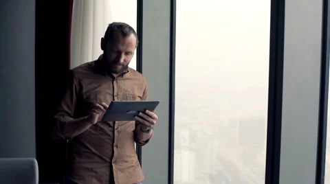 Young man with tablet computer standing by window at home Stock Footage 63302722