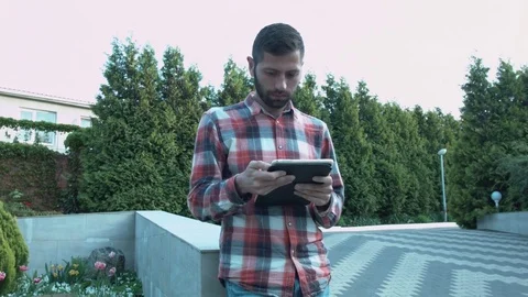 A young man with a tablet in his hands is leaning on the parapet in the park Stock Footage 75722061