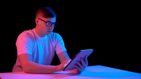 Young man with a tablet. A man is using a tablet. Blue and red light falls on a Stock Footage 125546901