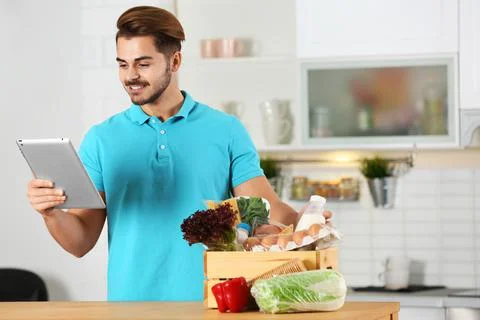 Young man with tablet PC and products in kitchen. Food delivery service Stock-Fotos