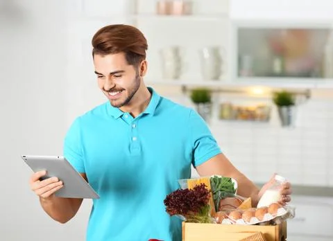 Young man with tablet PC and products in kitchen. Food delivery service Stock-Fotos