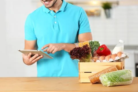 Young man with tablet PC and products in kitchen. Food delivery service Stock-Fotos