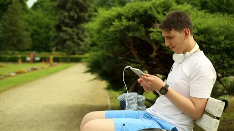 Young man with tablet sits on a bench at the park Video stock 64285280