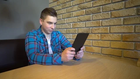 A young man with a tablet sits at a table. A man sits at home at a table with a Stock Footage 126354057