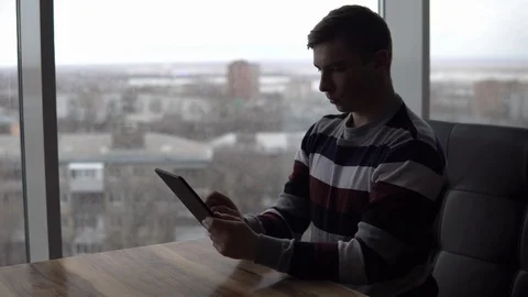 A young man with a tablet sits at a table. A man sits in a cafe by the panoramic Stock Footage 127252714
