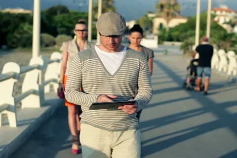 Young man with tablet walking along pier, women in background 스톡 동영상 12579293