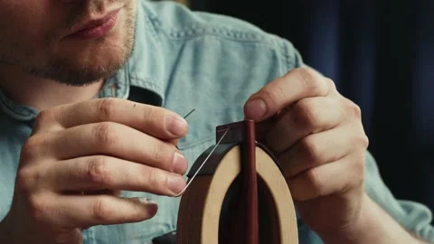 Young man tailor sewing two pieces of leather on stand close-up, using Stock Footage 157128885