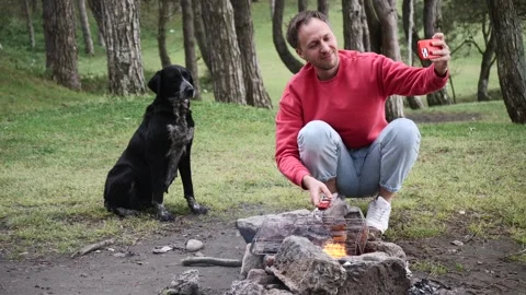 Young man take selfie with dog and roast meat on fire, picnic with pet in nature Stock Footage 242586391