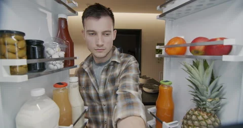 A young man takes a container with breakfast from the refrigerator. View from Stock Footage 249601932