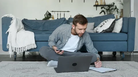 A Young Man Takes Notes on Paper, A Freelancer Works At Home, Uses A Laptop Stock Footage 156963030