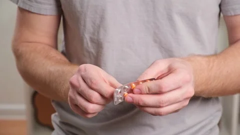 A young man takes out a tablet, pill from a blister pack. The concept of health Stock Footage 237858540