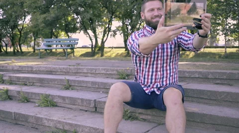 Young man takes selfie by tablet, sitting on stairs. Vidéo 67242876