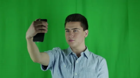 Young man takes selfies and smiles in front of a greenscreen in a blue shirt Stock Footage 59084746