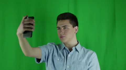 Young man takes selfies in front of a greenscreen in a blue shirt Vidéo 59084179