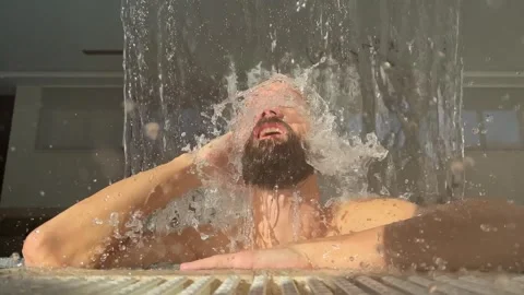 Young man takes a shower while standing under an artificial waterfall with hydro Stock Footage 259316276