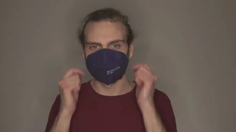 Young man taking off blue face mask in front of grey wall Stock Footage 146698321