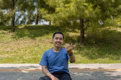 Young Man Taking a Break on a Pathway in a Green Park, Smiling and Inviting.. Stock Photos