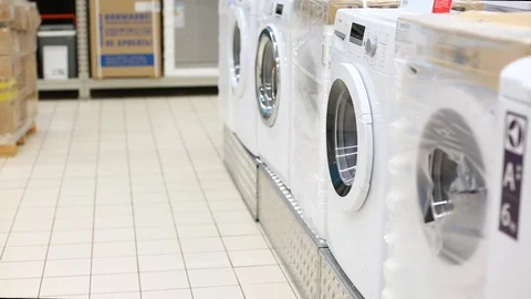Young man taking clothes out of washing machine in big store. Comic video Stock Footage 107342331