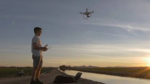 Young man taking off drone and flying it along river at sunset Stock Footage 111310219