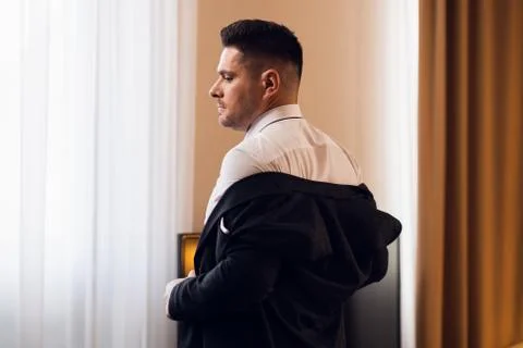 A young man taking off his jacket in a hotel room, rear view Stock Photos