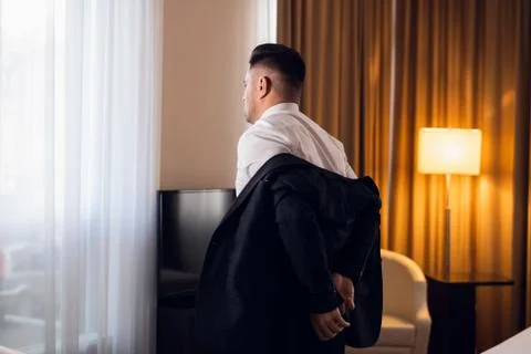 A young man taking off his jacket in a hotel room, rear view Stock Photos