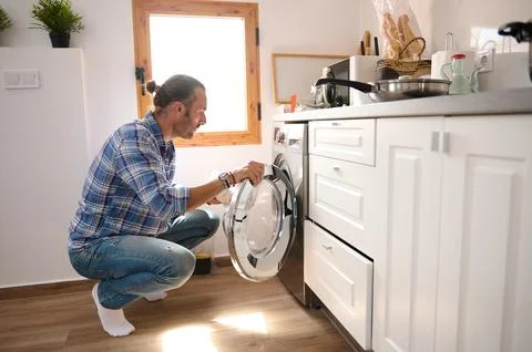 Young man taking laundry out of washing machine at home. Housekeeping, hous.. 스톡 사진