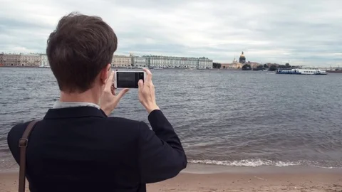 Young man taking photo using smartphone standing on seafront in city Stock Footage 80063603