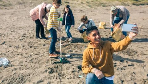 Young man taking selfie to group of volunteers cleaning beach Stock Photos
