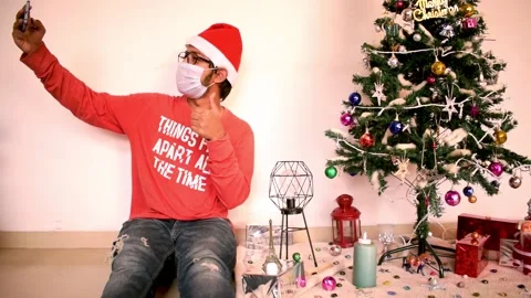 Young man taking selfie mobile smartphone with Christmas tree in mask santa hat Stock Footage 145181767