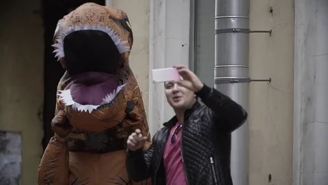 Young man taking selfie with person in dino mascot costume at city street Stock Footage 84932350