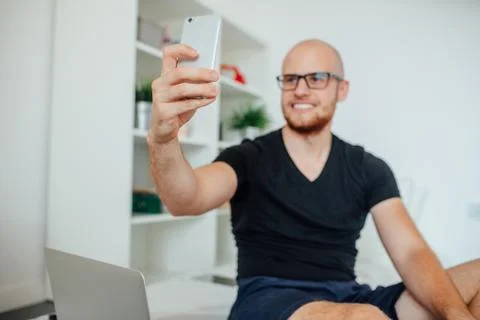 Young man is taking a selfie while sitting on bed. Home background Stock Photos