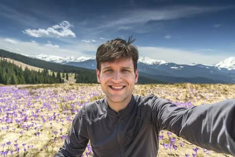 Young man taking selfie while sitting on mountainside full of purple crocuses Stock Photos
