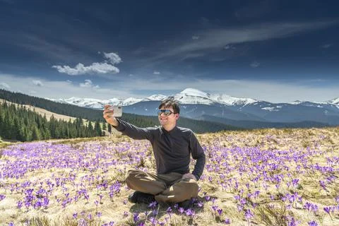 Young man taking selfie while sitting on mountainside full of purple crocuses Stock Photos