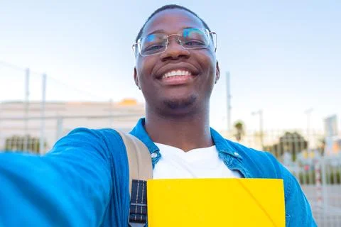 Young man taking a selfie while holding a yellow folder outdoors with glasses Stock Photos