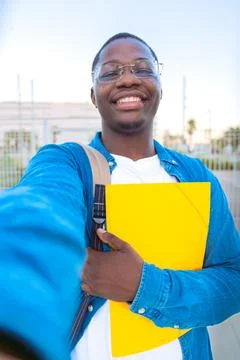 Young man taking a selfie while holding a yellow folder outdoors with glasses Stock-Fotos