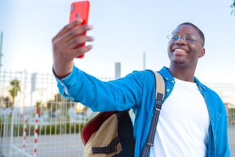 Young man taking a selfie while holding a yellow folder outdoors with glasses Stock Photos