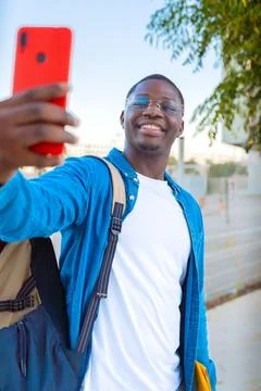Young man taking a selfie while holding a yellow folder outdoors with glasses Stock-Fotos