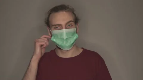 Young man taking off surgical face mask in front of grey wall Stock Footage 146698405