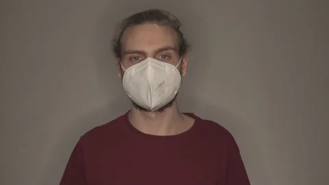 Young man taking off white face mask in front of grey wall Stock Footage 146698275