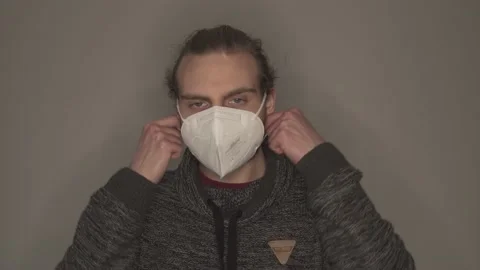 Young man taking off white face mask in front of grey wall Stock Footage 146698599