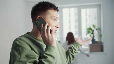 The young man is talking briskly on the phone. In the background, a girl wanders Stock Footage 151498047