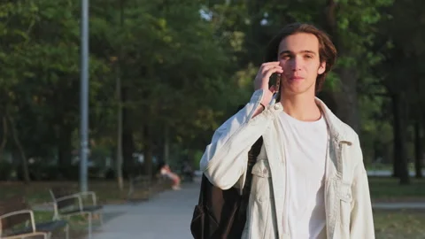 Young man is talking on a cell phone while walking down the street.  Positive Stock Footage 201610758