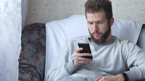 Young man talking on cellphone and drinking coffee on chair at home Stock Footage 68753638